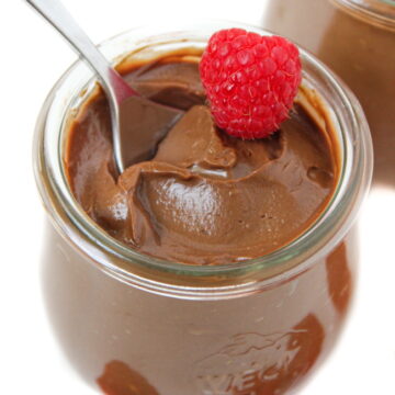 Vegan avocado chocolate mousse in a small glass jar with fresh raspberry on top