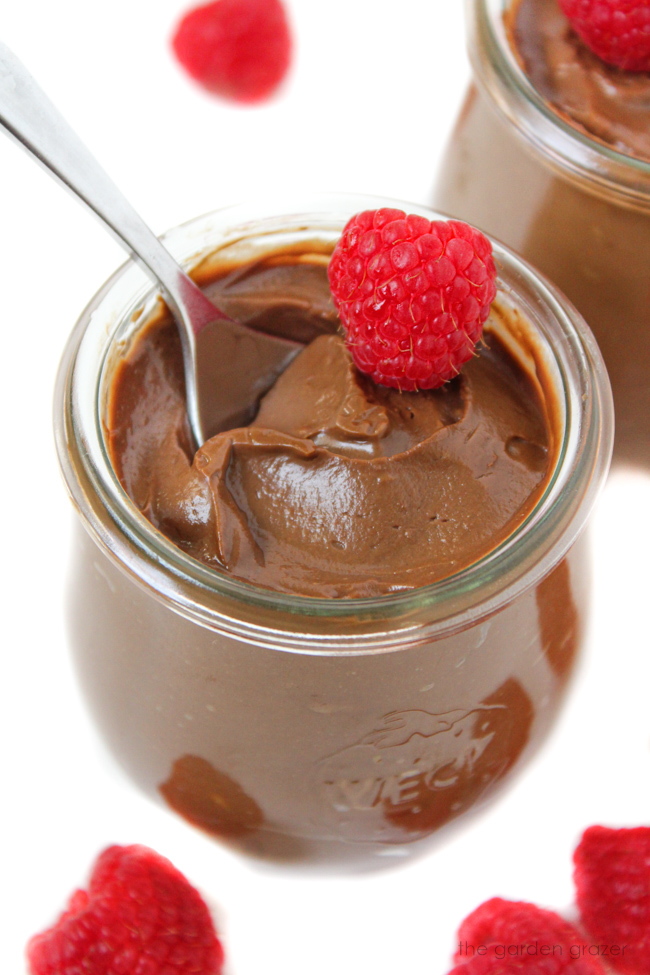 Vegan avocado chocolate mousse in a small glass jar with fresh raspberry on top