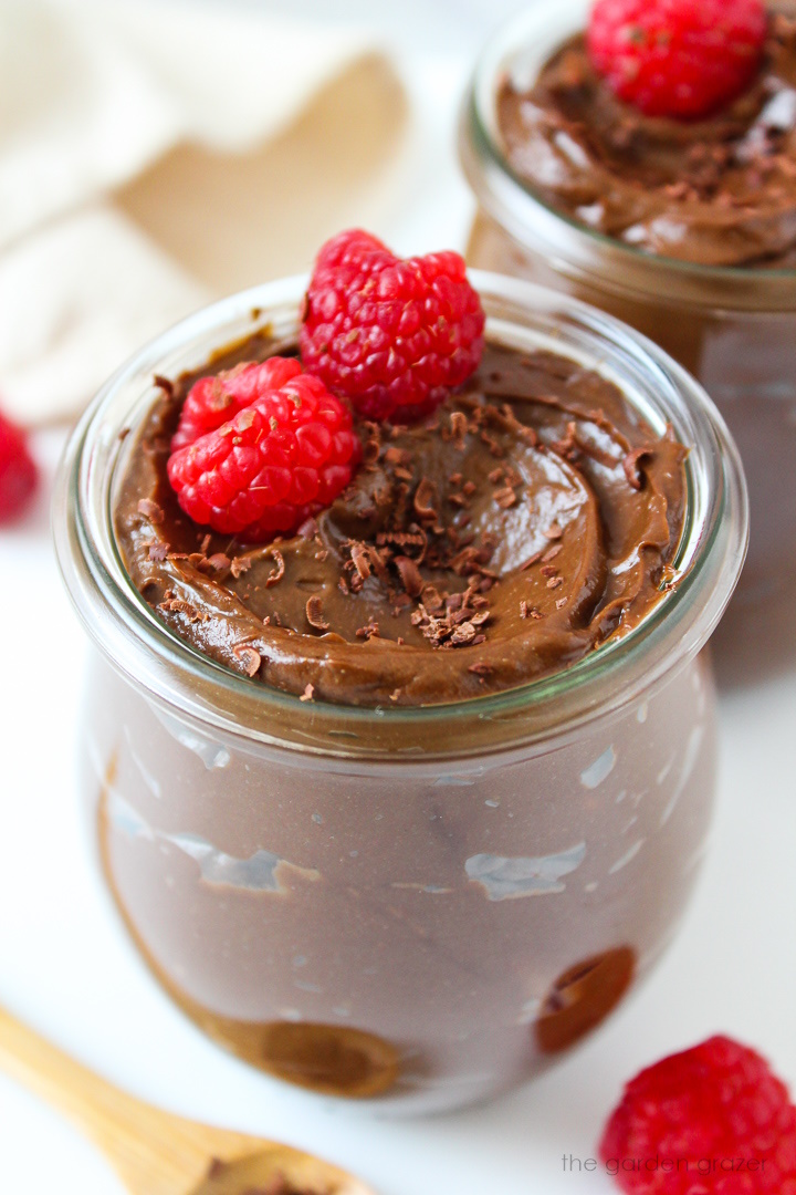 Close up view of vegan avocado chocolate mousse in a small glass serving jar topped with raspberries