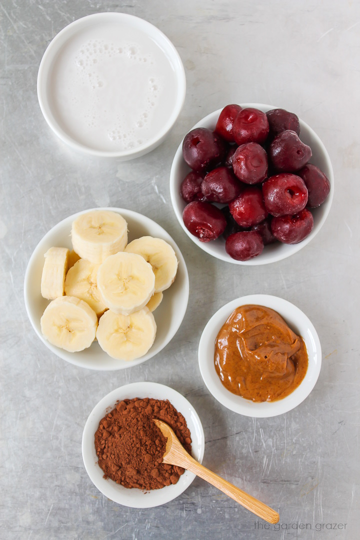 Frozen cherries, banana, dairy-free milk, almond butter, and cocoa powder ingredients laid out on a metal tray