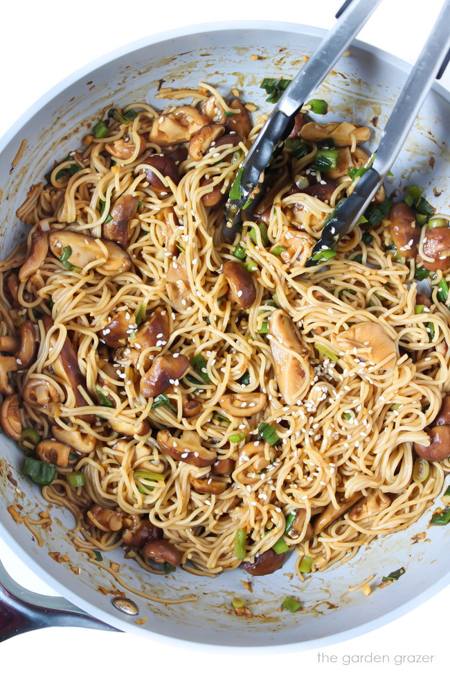 Vegan noodles and mushrooms cooking in a skillet with an Asian-style sauce