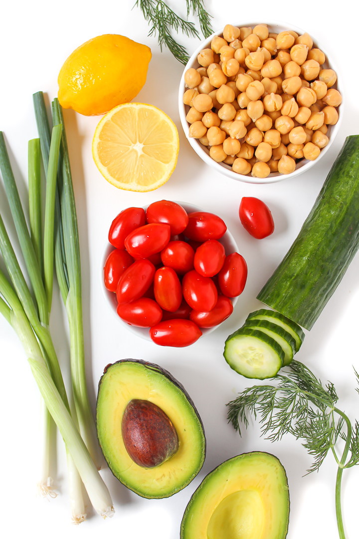 Cucumber, tomato, lemon, dill, and avocado ingredients on a white table