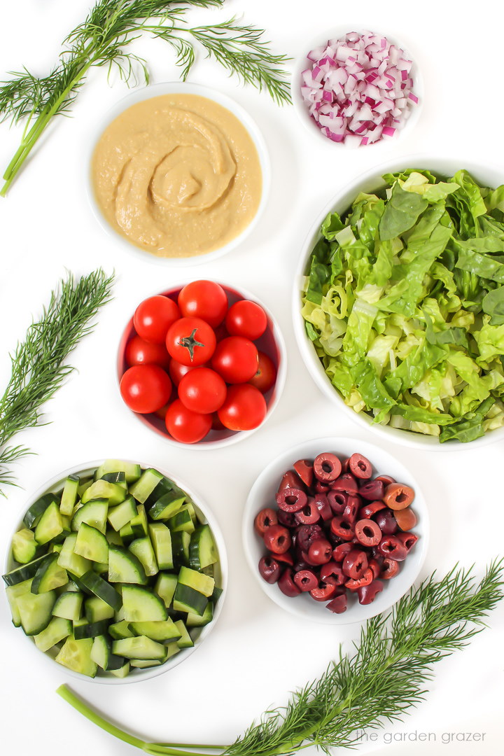 Romaine lettuce, tomatoes, dill, olives, onion, cucumber ingredients on a white table