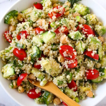 Overhead view of quinoa chickpea salad with dill in a white serving bowl with spoon