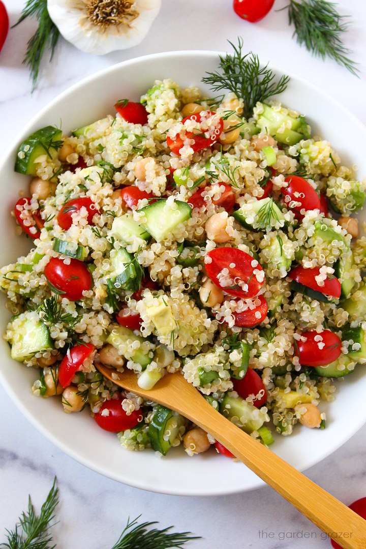 Overhead view of quinoa chickpea salad with dill in a white serving bowl with spoon
