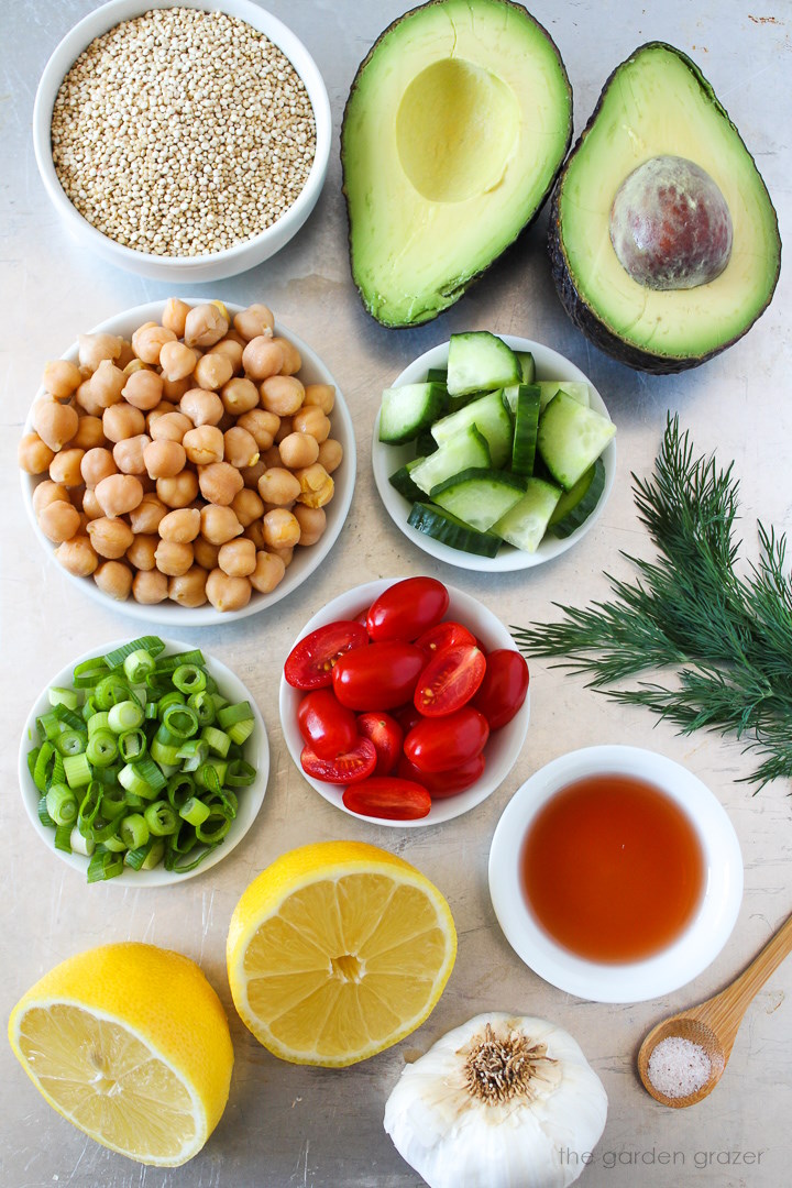 Garbanzo beans, avocado, cucumber, tomato, green onion, fresh dill, lemon, and vinegar ingredients laid out on a metal tray