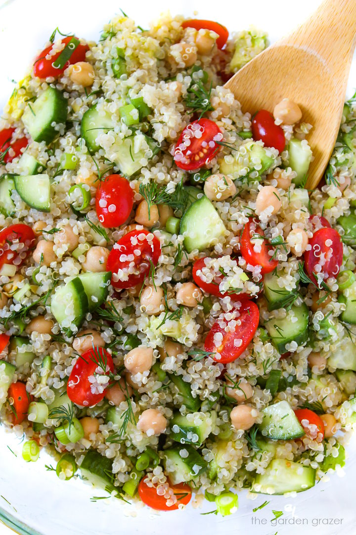 Preparing quinoa chickpea salad in a large glass bowl with wooden mixing spoon