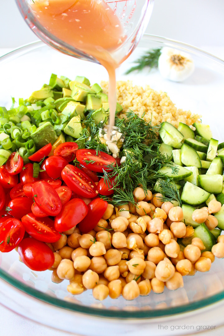 Lemon vinegar dressing being poured over salad ingredients in a large glass bowl