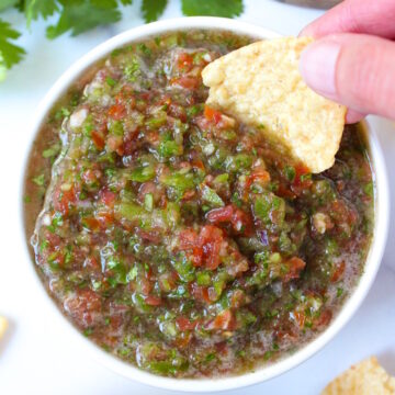 A tortilla chip dipping into a bowl of fresh garden salsa