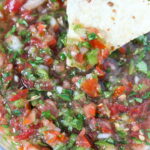 Tortilla chip dipping into a bowl of fresh salsa