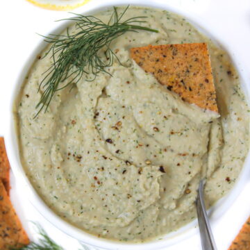 Fresh lemon dill hummus in a white bowl with serving spoon and crackers