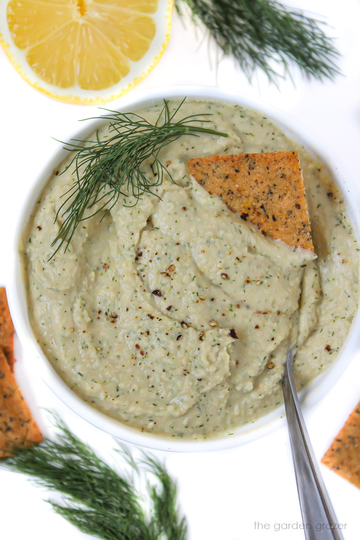 Fresh lemon dill hummus in a white bowl with serving spoon and crackers