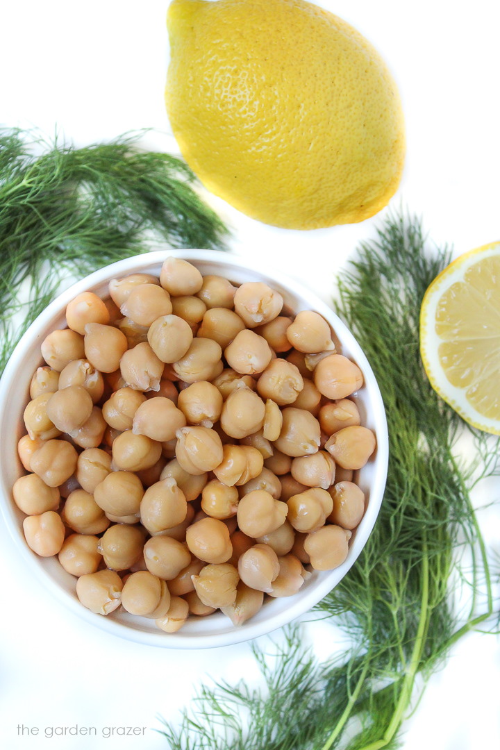 Chickpeas, fresh dill, and lemon ingredients on a white table