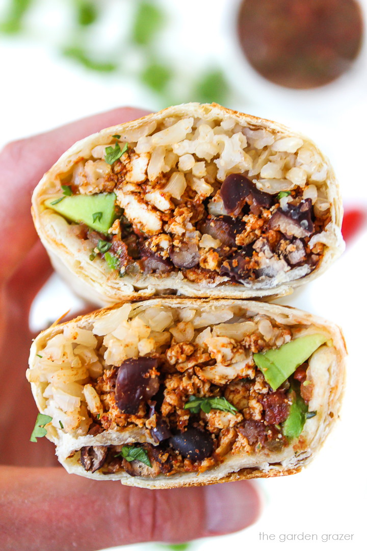 Hand holding a tofu black bean burrito cut in half