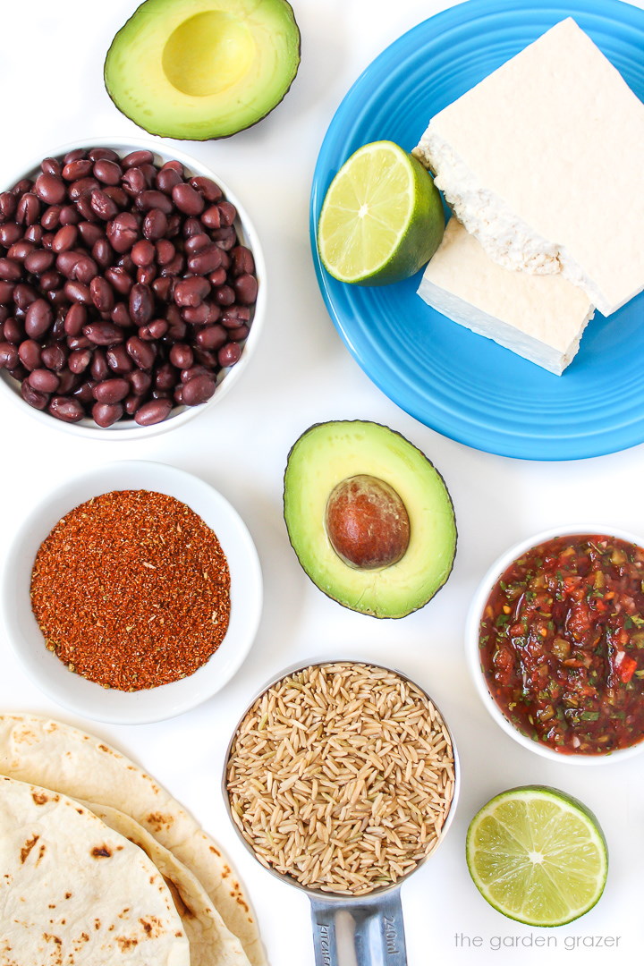 Black beans, avocado, rice, salsa, lime, and taco seasoning ingredients on a white table