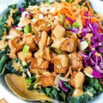 Asian Kale Salad with baked tofu and cabbage in a white bowl topped with peanut dressing