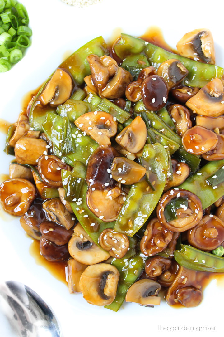 White plate of vegan teriyaki mushrooms and snow peas with sesame seeds