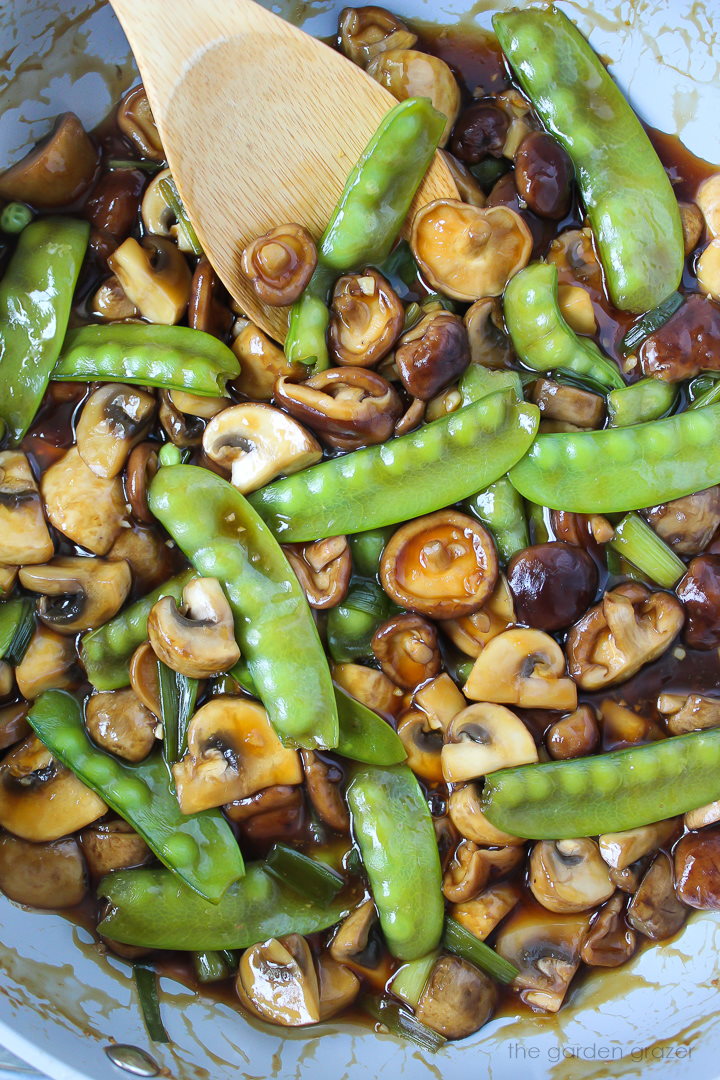 A large skillet of mushrooms and peas cooking in sauce