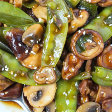 Close-up view of saucy mushrooms and snow peas on a white plate with spoon