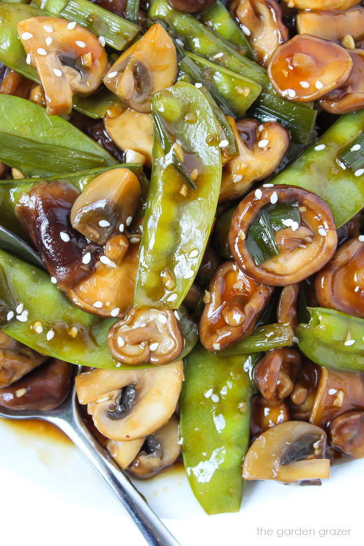 Close-up view of saucy mushrooms and snow peas on a white plate with spoon