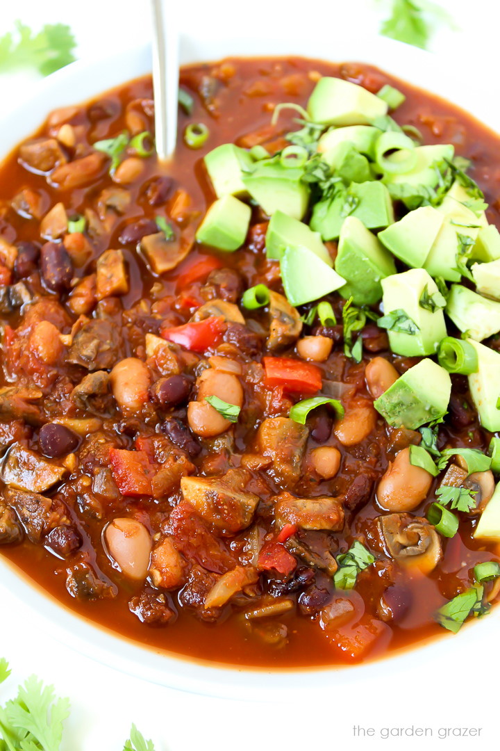 White bowl of vegan chili topped with diced avocado and cilantro