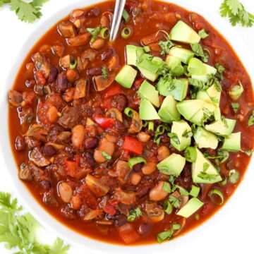 Mushroom chili in a white bowl topped with avocado and cilantro