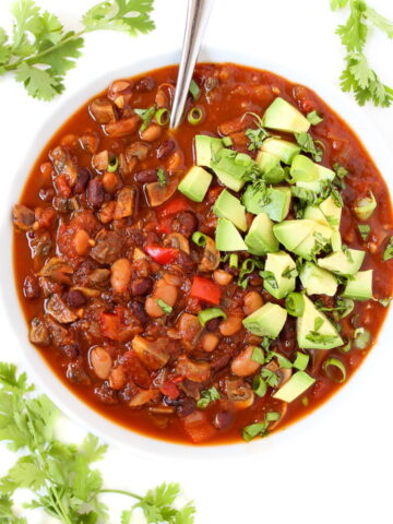 Mushroom chili in a white bowl topped with avocado and cilantro
