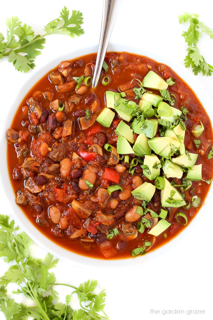 Mushroom chili in a white bowl topped with avocado and cilantro