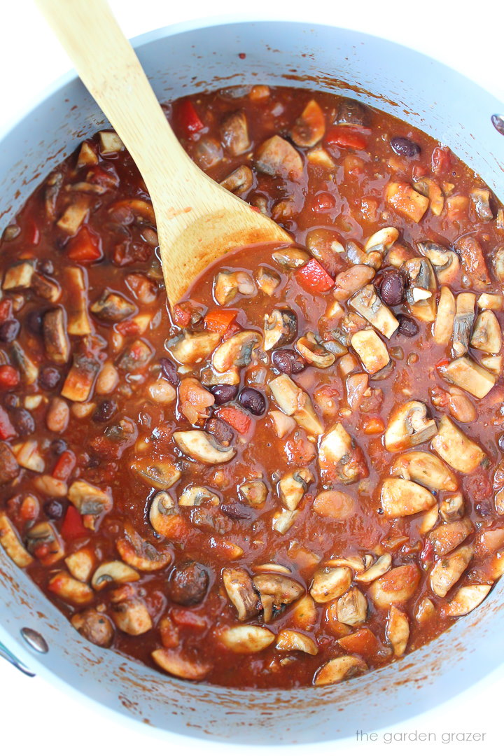 Vegan mushroom and bean chili cooking in a large pot with wooden spoon