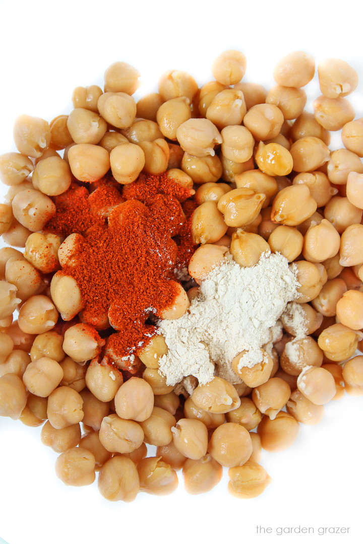 Chickpeas in a bowl with spices on top before mixing