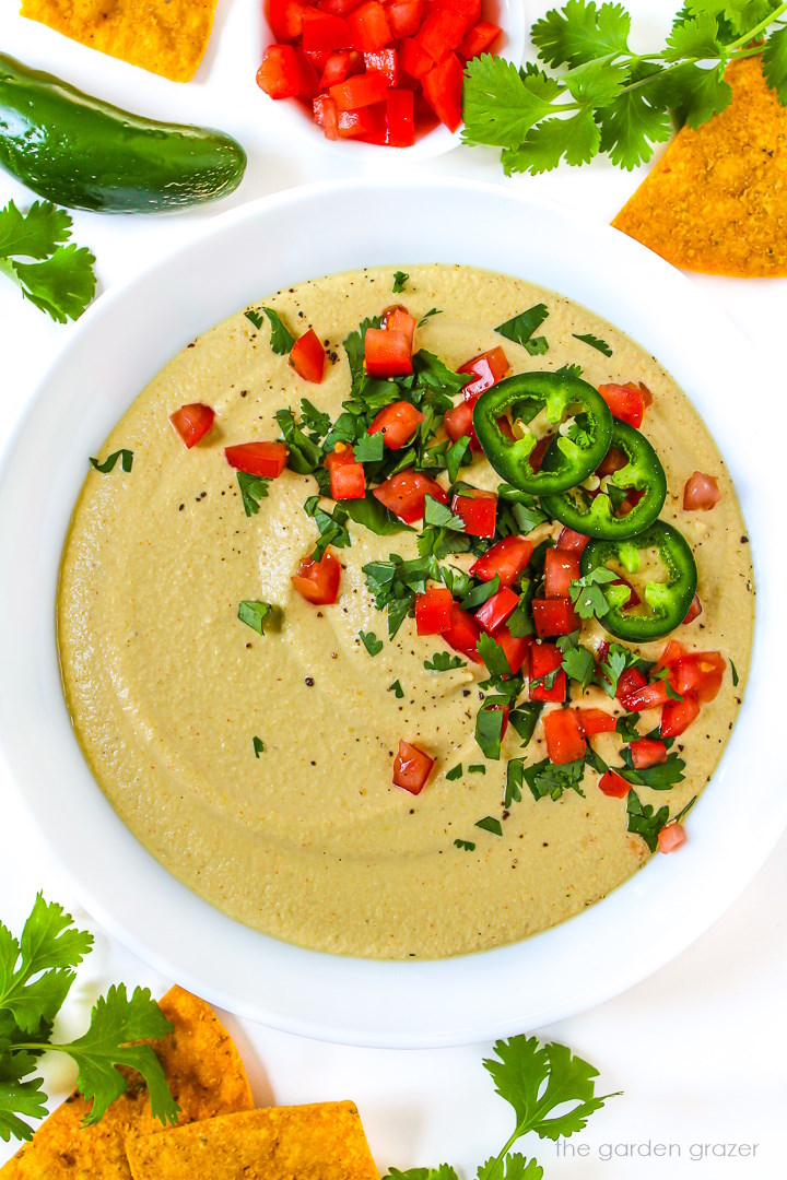 Vegan cashew queso in a white serving bowl topped with fresh cilantro, tomato, and jalapeno