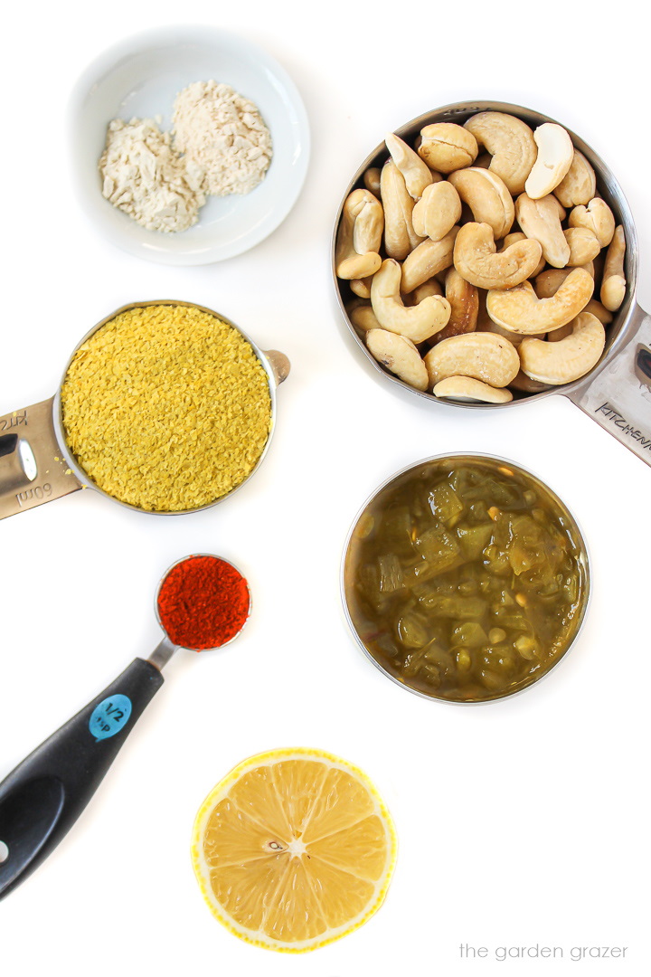 Raw cashews, nutritional yeast, diced chiles, and spice ingredients laid out on a white table