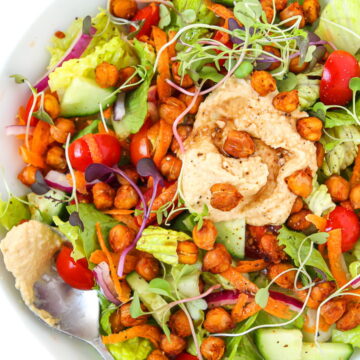 Overhead view of roasted chickpea hummus salad in a white bowl with spoon