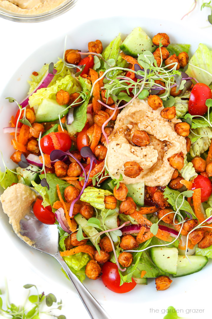 Romaine lettuce salad in a white bowl topped with hummus and roasted chickpeas