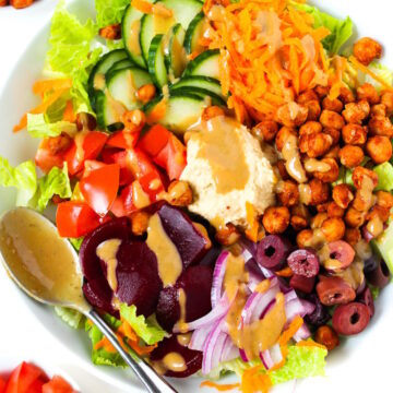 Roasted chickpea salad served in a white bowl topped with hummus and balsamic dressing