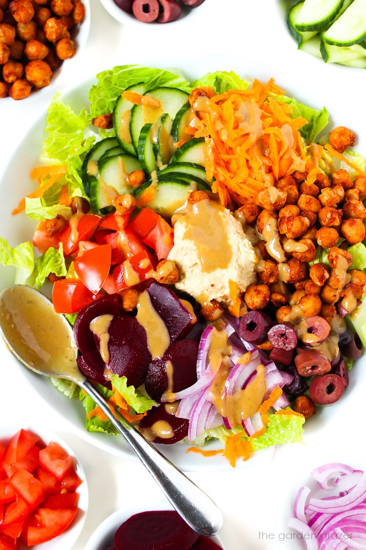 Roasted chickpea salad served in a white bowl topped with hummus and balsamic dressing