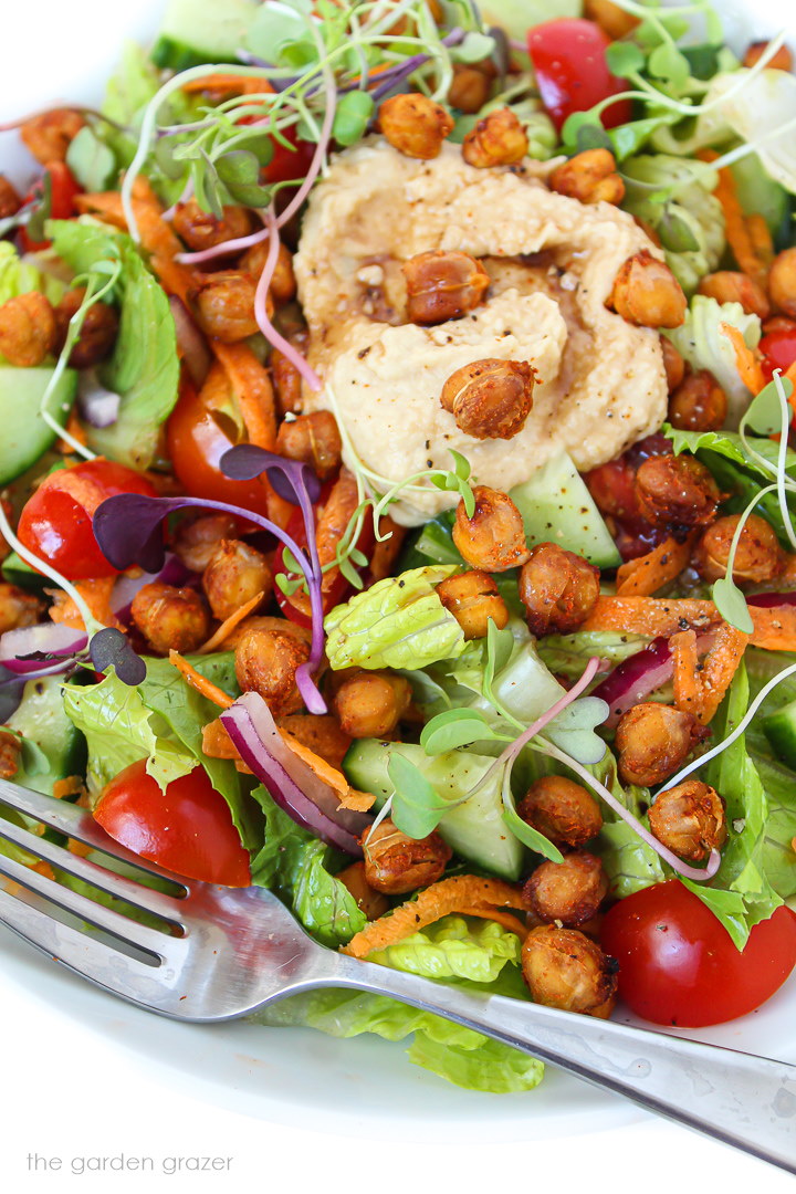 Close up view of roasted chickpea salad with hummus on a white plate