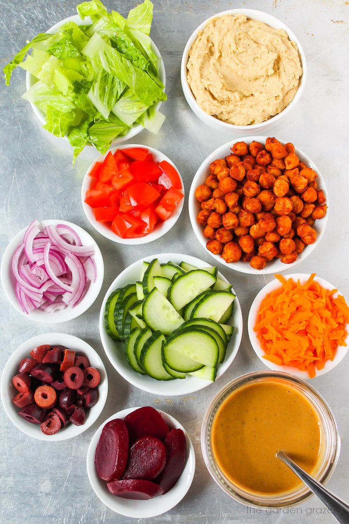 Romaine lettuce, hummus, tomato, red onion, cucumber, carrot, and dressing ingredients laid out on a metal tray