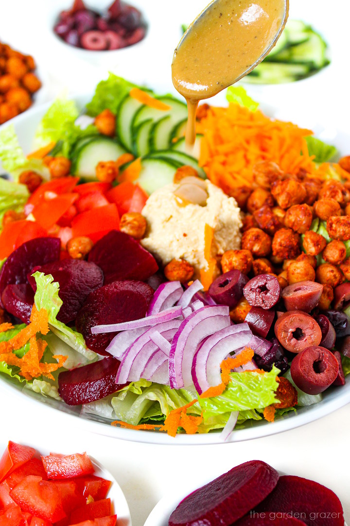 Balsamic dressing being spooned over prepared roasted chickpea salad in a white bowl