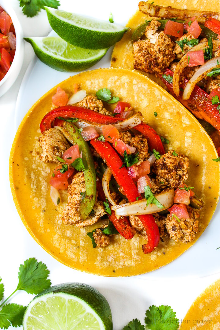 Close up view of tofu fajitas served on a white plate with cilantro and salsa