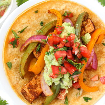 Tofu fajitas on a white plate topped with guacamole and salsa