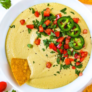 Overhead view of cashew queso in a white serving bowl with chips garnished with cilantro and tomato