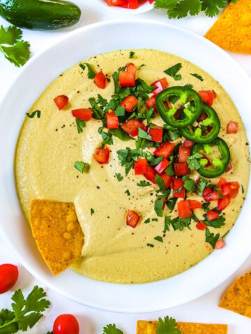 Overhead view of cashew queso in a white serving bowl with chips garnished with cilantro and tomato
