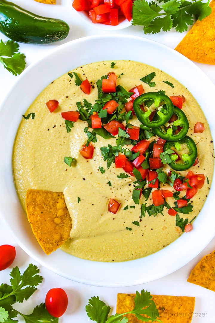 Overhead view of cashew queso in a white serving bowl with chips garnished with cilantro and tomato