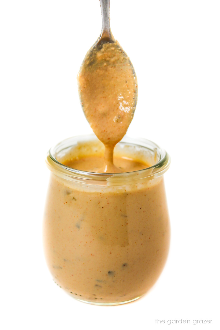 Spoon dipping into a small glass jar of vegan big mac sauce