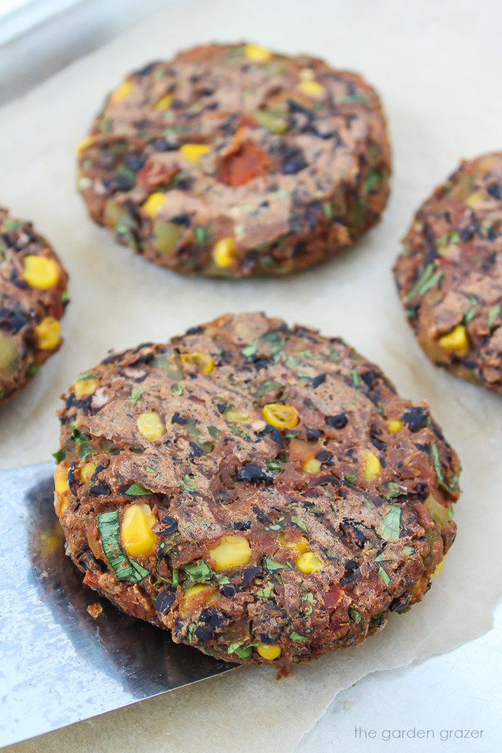 Vegan black bean burgers cooking on a baking sheet with metal spatula