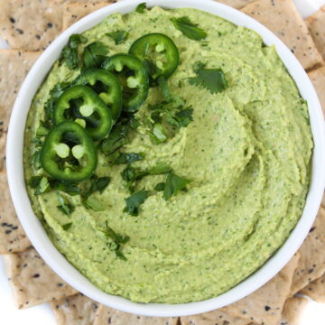 Cilantro jalapeno hummus in a white bowl surrounded with crackers