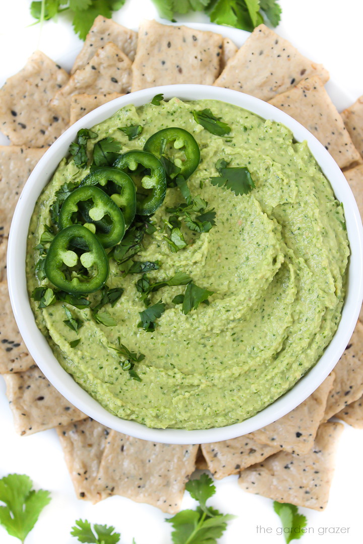 Cilantro jalapeno hummus in a white bowl surrounded with crackers