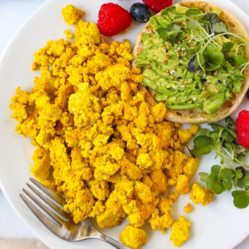 Overhead view of eggy tofu served on a white plate with fresh berries and avocado toast
