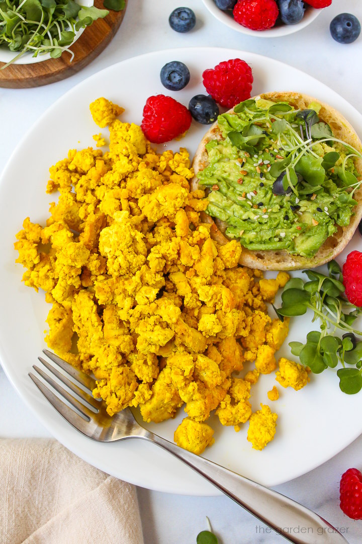Overhead view of eggy tofu served on a white plate with fresh berries and avocado toast